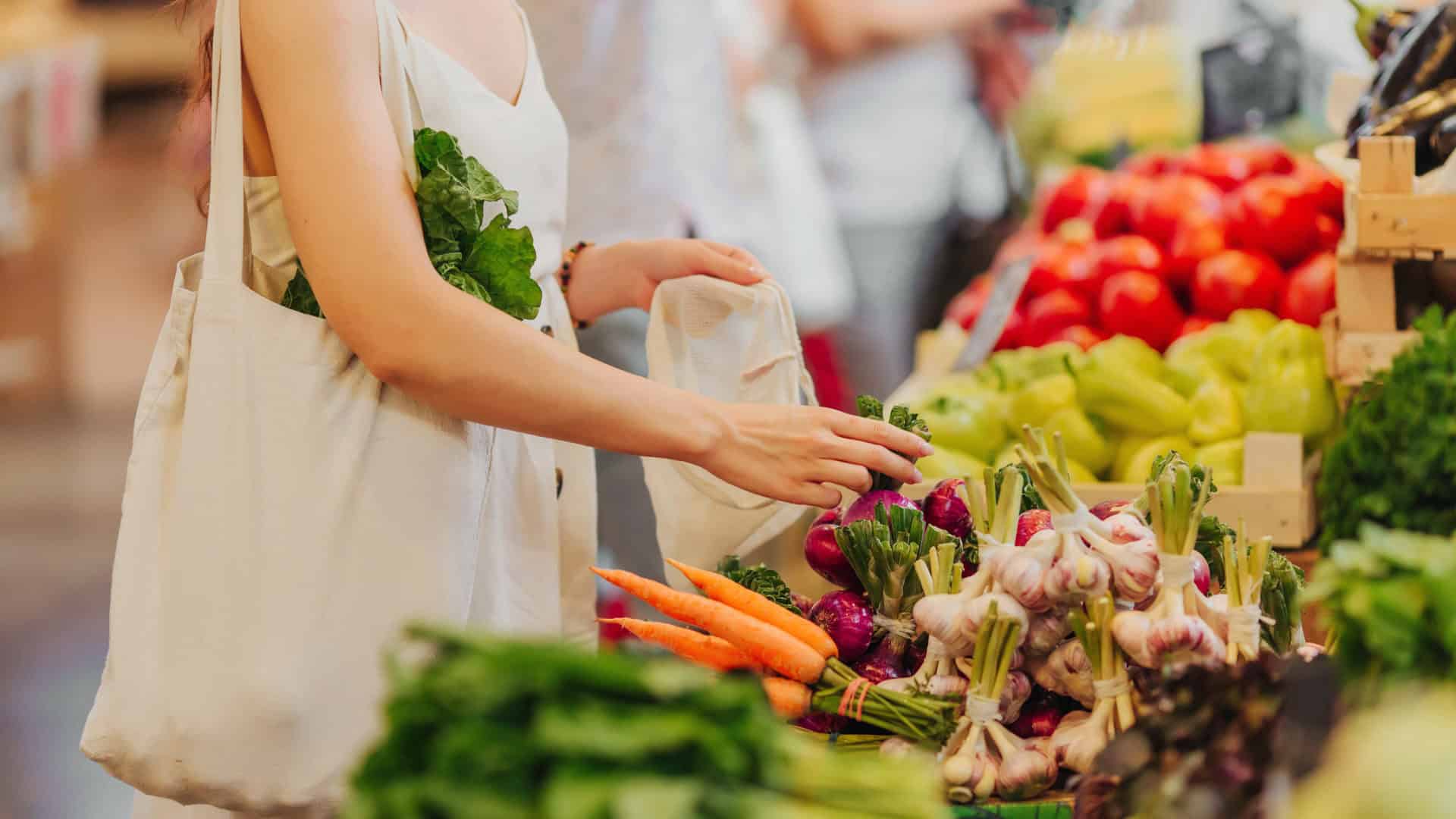 female hands puts fruits and vegetables in cotton produce bag at food market. reusable eco bag for shopping. zero waste concept.